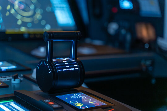 Engine telegraph close-up with ECDIS display in background blue light