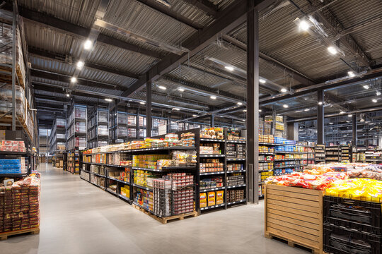 Modern spacious supermarket interior with high ceilings and industrial design. Wide aisles with shelves full of groceries and food products. Large grocery store or warehouse market