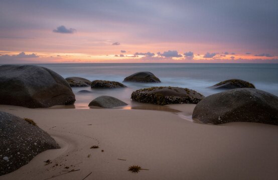A tranquil beach scene at sunset with smooth rocks and a calm sea.