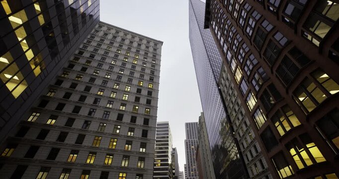 looking upward between towering skyscrapers, dramatic vertical perspective with lit window grids, sense of ambition and upward mobility, architect and developer