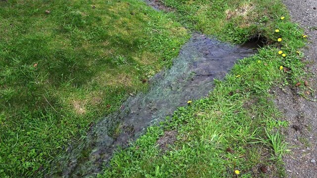 Water running out of black plastic stormwater system pipe and into grass ditch
