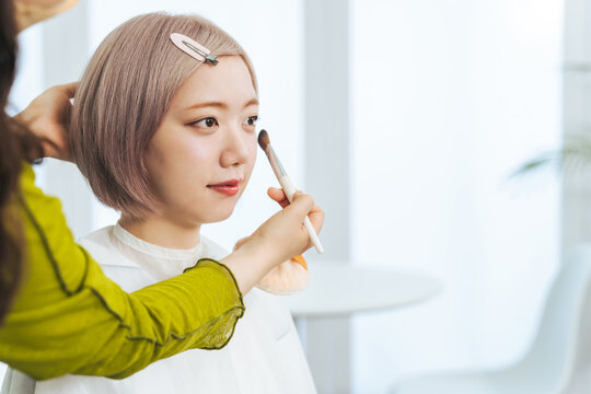 メイクしてもらうハイトーンヘアの女性