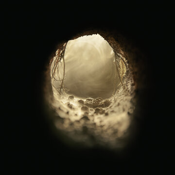 Inside an underground dirt cave filled with an eerie fog. Mysterious subterranean tunnel opening into lighted passage filled with a light haze. Spooky old burrow, sewer, or dugout.