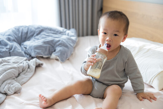 Baby sitting on bed drinking milk bottle