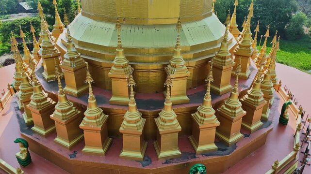 A stunning close-up drone shot of Maha Chedi Sri Sarakham, Thailand, featuring golden architecture against a beautiful sunset backlight.