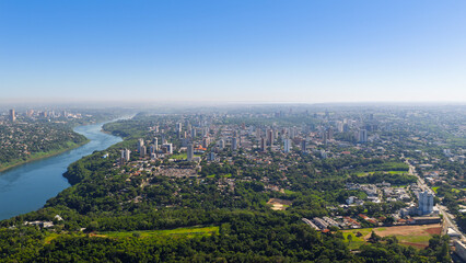 Aerial panorama of Foz do Iguaçu skyline framed by lush greenery and the Paraná River flowing toward Paraguay. © Marcio Eneas