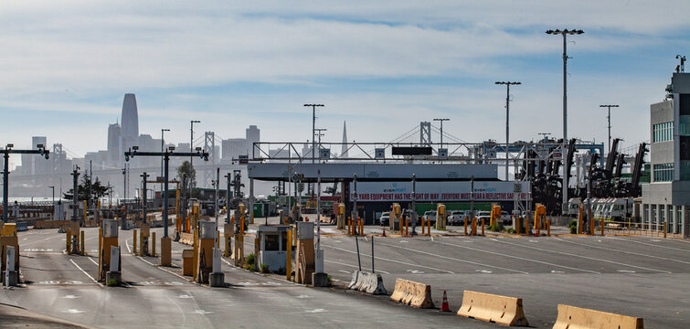 Port of Oakland shipping facility with expansive container yard infrastructure, industrial freight operations, and the distant San Francisco skyline rising beyond the Bay Area maritime logistics corri