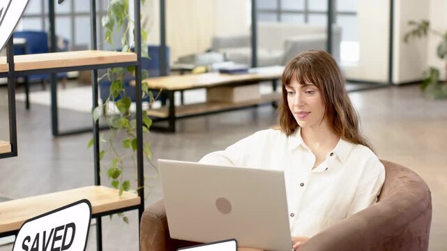 Mid-adult woman working on laptop in business lounge, feedback bubbles sliding in, tracking likes