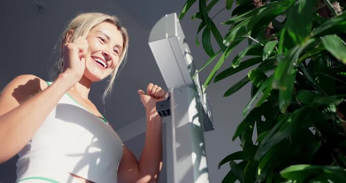 Female athlete standing on electronic scales weighing herself in modern gym