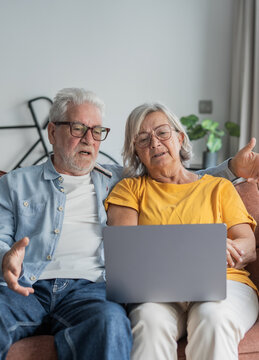 An older couple relaxes on their sofa while sharing a laptop, looking engaged as they browse, video chat, or learn online &mdash; capturing companionship, technology use, and everyday home life.