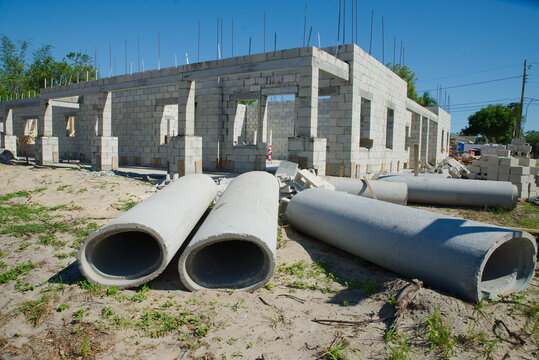 Construction Site With Concrete culvert pipes lie on a grassy lot in front of a partially built cinderblock building, conveying construction progress, materials and infrastructure work on a suburban d