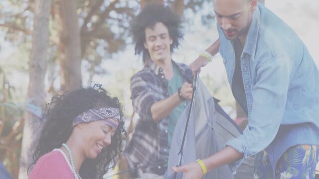 Three friends unfolding gray tent in park, coordinating poles and clips while preparing campsite