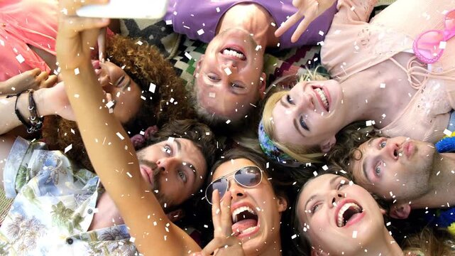 Friends lying heads together raising smartphone posing playfully as confetti falls for social media