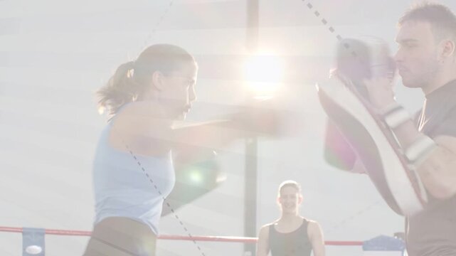 Female trainee throwing jabs toward coach mitts after coach signaling, training boxing under glare