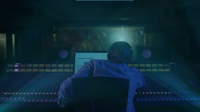 Male audio engineer getting live take cue, tweaking faders, watching animated meters, raising arms