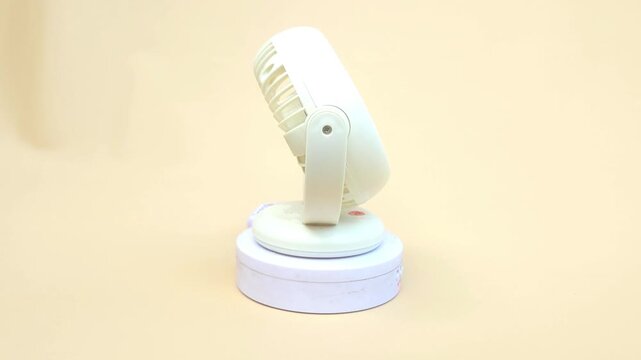 Close-up of a compact, portable mini fan displayed on a turntable against a soft yellow background. Ideal for personal cooling at home, in the office, or while traveling. Perfect for use in advertisin