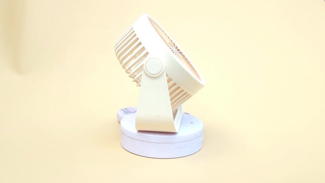 Close-up of a compact, portable mini fan displayed on a turntable against a soft yellow background. Ideal for personal cooling at home, in the office, or while traveling. Perfect for use in advertisin