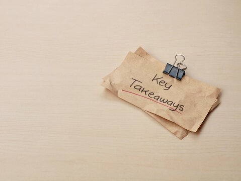 Key takeaways handwritten on brown paper with binder clip on wooden desk. Perfect for business, education, and summary-related concepts