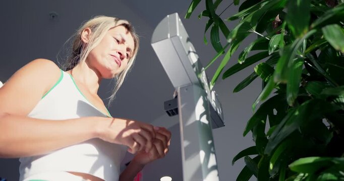Female athlete standing on electronic scales weighing herself in modern gym