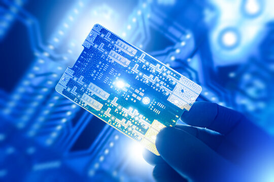 Microelectronics manufacturing inspection. Gloved hand holds advanced printed circuit board, evaluates semiconductor components, supports chip design testing and high-tech hardware development.
