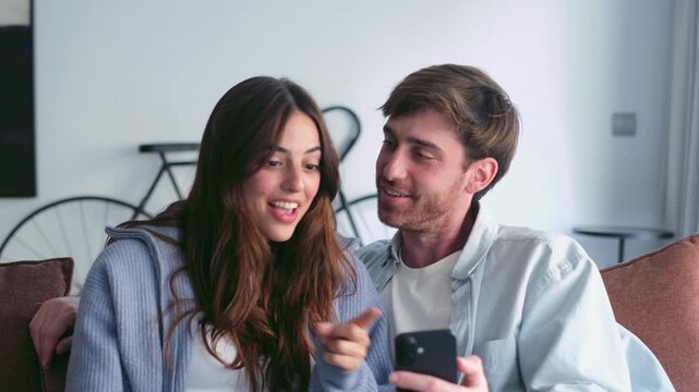 Happy Young Couple Enjoys a Video Call on Smartphone, Expressing Joy and Surprise While Relaxing on Sofa