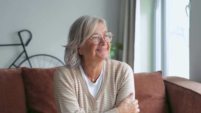 Smiling Senior Woman with Glasses Looking at the Camera on a Couch at Home