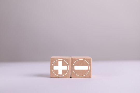 Wooden blocks with green plus and red minus symbols are placed on a wooden table, representing advantages and disadvantages risk assessment, evaluation, selection, comparison and business strategies.