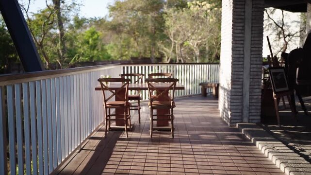 A cozy veranda scene with dining table, chairs, and a painting on a wooden stand. Morning sunlight streams through the railing, creating warm tones and a calm, inviting home atmosphere.