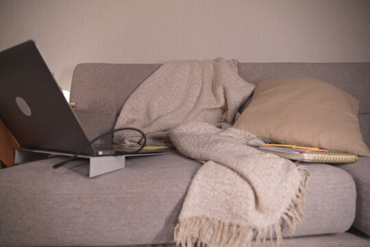 Laptop, blanket, and pillow resting on a comfortable sofa for remote work or studying