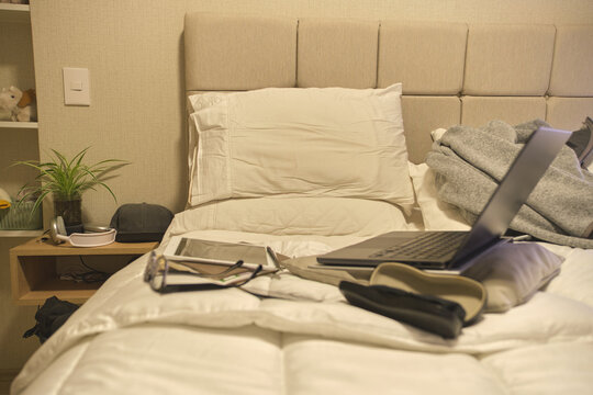 Bedroom with a comfortable bed, laptop, headphones, tablet, and glasses representing a study space