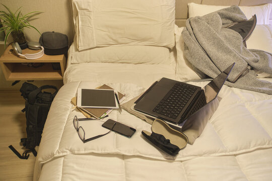 Bed acting as a messy home office with devices and notes for remote work