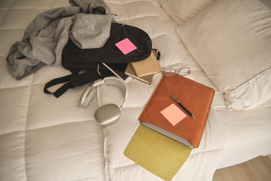 Student backpack, headphones, and study materials lying on a white bed