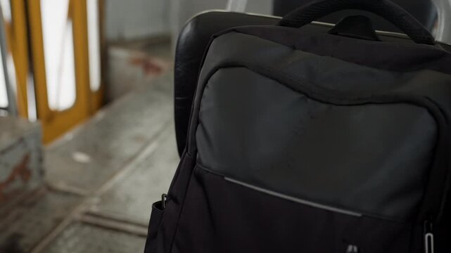 Black backpack on metal stairs, closeup at urban station showing worn concrete, yellow railing and tiled platform nylon daypack with zipper pocket and padded handle, moody morning light, commuters