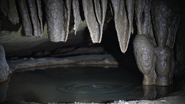 Cave formations with stalactites and stalagmites over water.