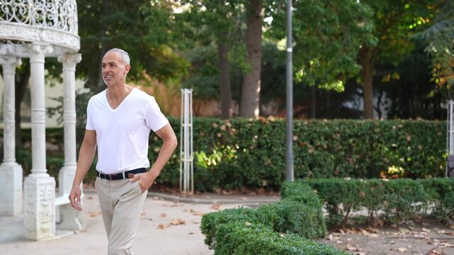 Man walks calmly through garden. Garden features white gazebo and green hedges. He smiles softly, enjoying the quiet atmosphere. Ideal for wellness or outdoor lifestyle imagery