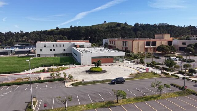 Aerial view of the modern architectural buildings and the nearly empty parking lot of Skyline College in San Bruno, California, on a sunny day with hills in the background