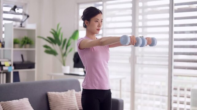 Asian adult woman exercising indoors using light dumbbells for home workout fitness health training wellbeing active lifestyle strength building modern apartment home gym