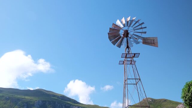 Spinning windpump (windmill) upwards view against blue sky with mountain in back
