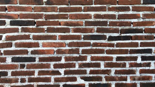 Weathered brick wall shows aged, rustic charm. Mortar lines reveal time's gentle wear. Red bricks stand strong, textured and worn. Ideal for vintage, industrial, or architectural themes. side view. 