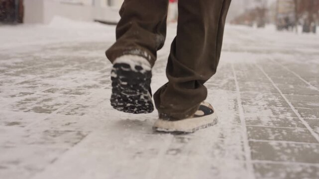Boot heels on icy city tiles, close low angle of tread and sole kicking through slush, brisk stride of urban messenger, blurred storefronts and snowflakes in background, emphasis on traction, motion
