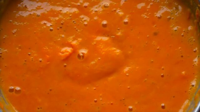pumpkin soup blending in blender close-up, thick orange puree spinning into vortex inside container, smooth texture forming during food preparation, healthy meal concept, minimal kitchen composition