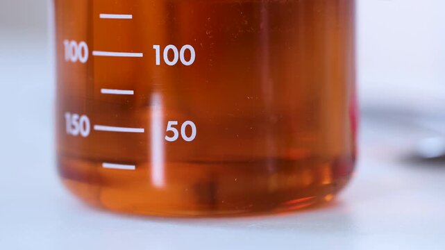 Laboratory beaker with orange liquid close up of glass measuring cylinder in chemistry lab.