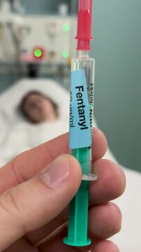 Close-up of a fentanyl syringe held in hand with a patient blurred in the background. Concept for medical treatment, pain management, and opioid use in healthcare.