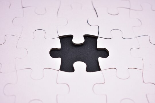 An incomplete white jigsaw puzzle featuring a single central void, symbolizing a missing element, problem-solving, or an unfinished task.