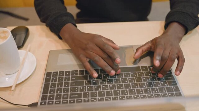 Black hands typing on laptop at desk, entrepreneur preparing presentation slides, cappuccino on saucer, wireless mouse nearby, focused fast typing, modern coworking vibe, bright professional energy
