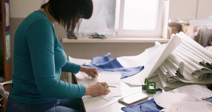 Tailor workshop. Fashion creation. Designer making paper pattern with professional tool. Woman measuring draft with curve ruler pencil on desk.