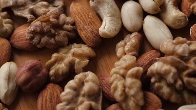 Close-up of whole peeled nuts mix on a wooden background. Appetizing assortment of almonds, cashews, hazelnuts, and walnuts rotating under warm light