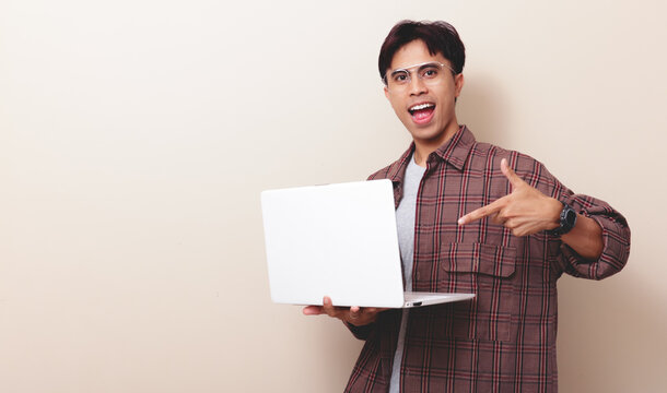 Excited young Southeast Asian IT professional in casual shirt working on laptop while pointing at screen. Digital lifestyle and tech success on isolated background.
