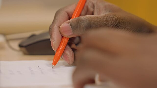Student fills answers with pen. Focused student writes answers on exam sheet during test. Concentrated student diligently completes exam answers using orange pen in quiet classroom environment