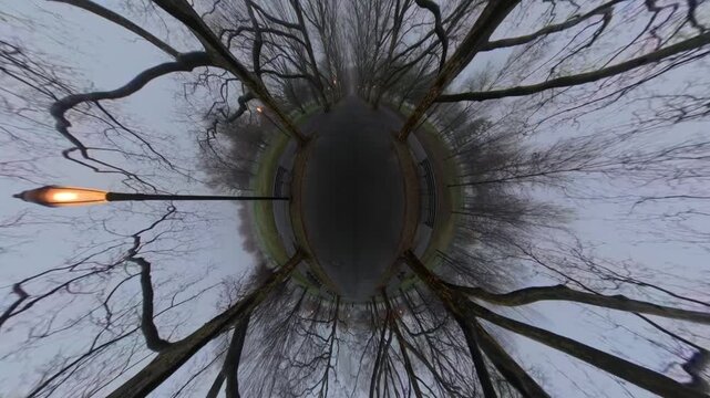 A top down, distorted view of a paved walkway in a park on a cloudy day. It was manipulated into a tiny planet. The camera is tilted down and dolly in along the path.